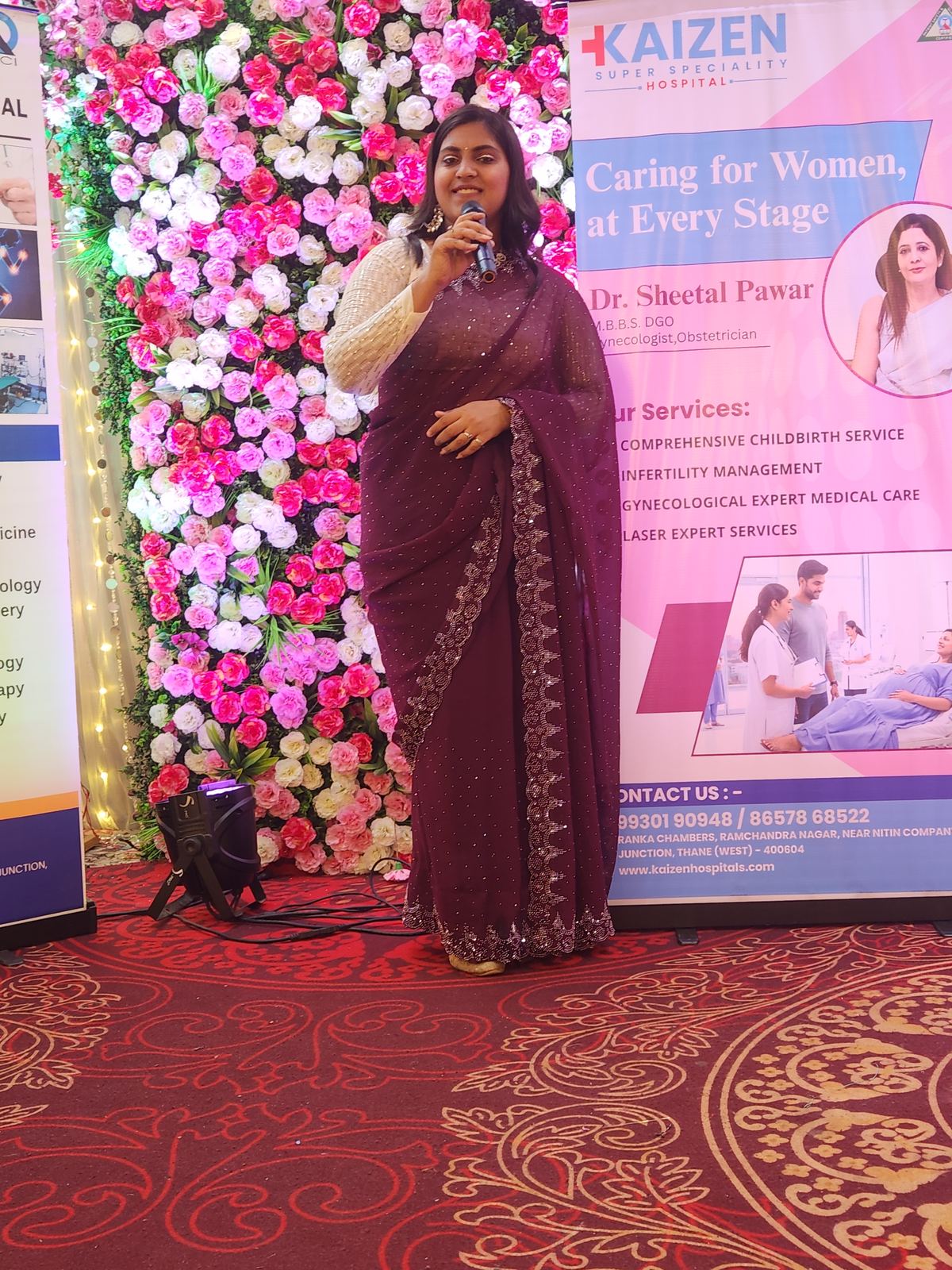 Anchor Ananya Kundu at a flower-wall corporate stage